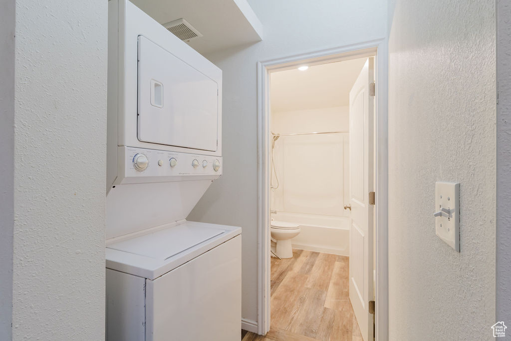 Laundry area featuring stacked washer / drying machine, light wood-style flooring, and a textured wall