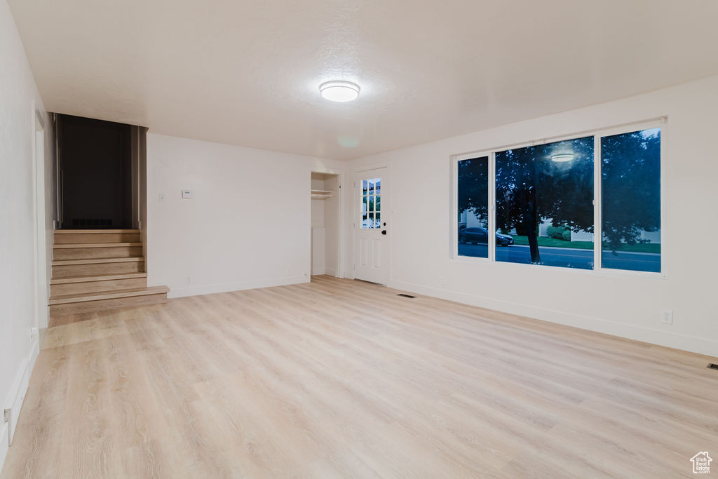 Unfurnished room with light wood-style flooring, stairs, and baseboards