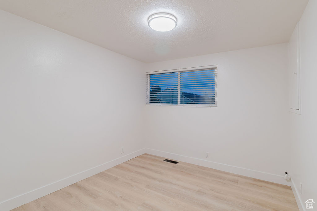 Unfurnished room with baseboards, light wood-style floors, and a textured ceiling