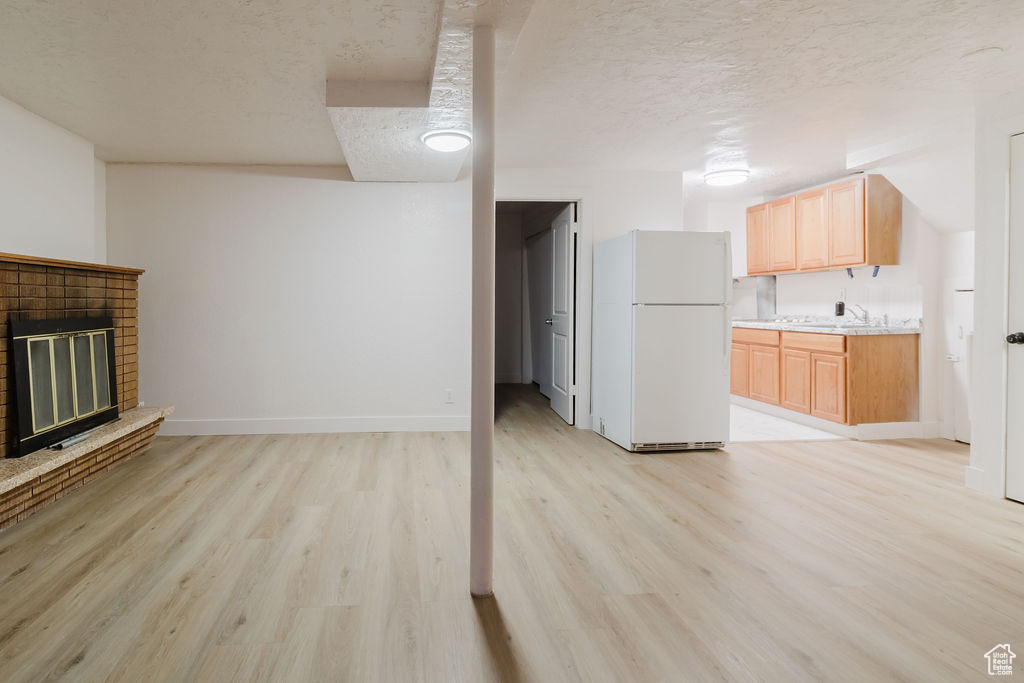 Unfurnished living room featuring light wood-style floors, a textured ceiling, a sink, baseboards, and a fireplace