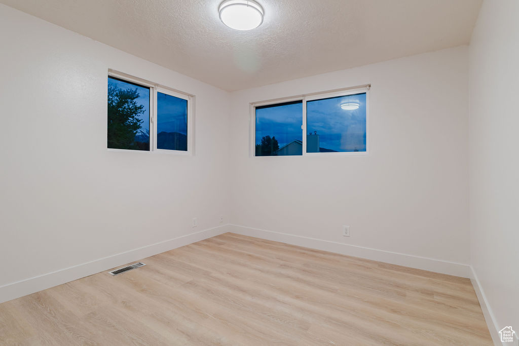 Spare room with light wood finished floors, a textured ceiling, and baseboards