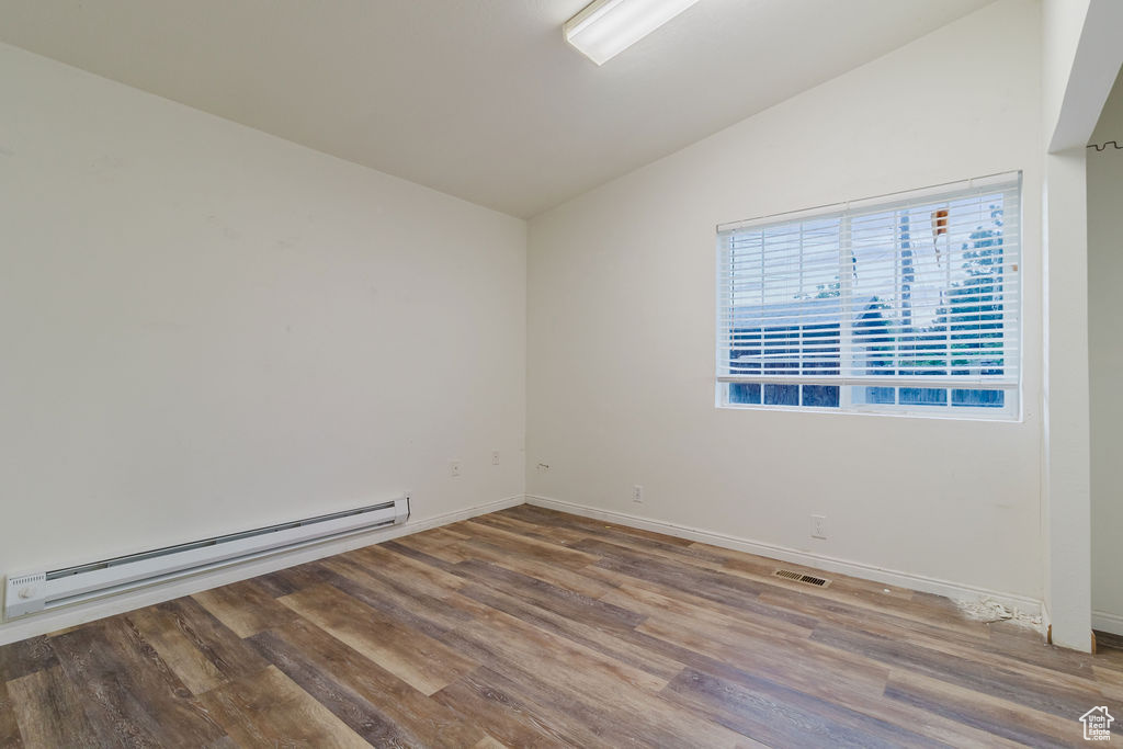 Spare room with a baseboard radiator, vaulted ceiling, wood finished floors, and baseboards