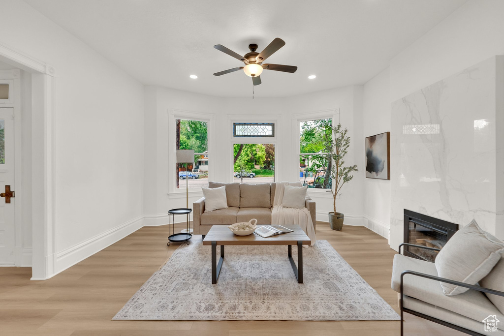 Living room featuring light wood-type flooring, a fireplace, baseboards, ceiling fan, and recessed lighting