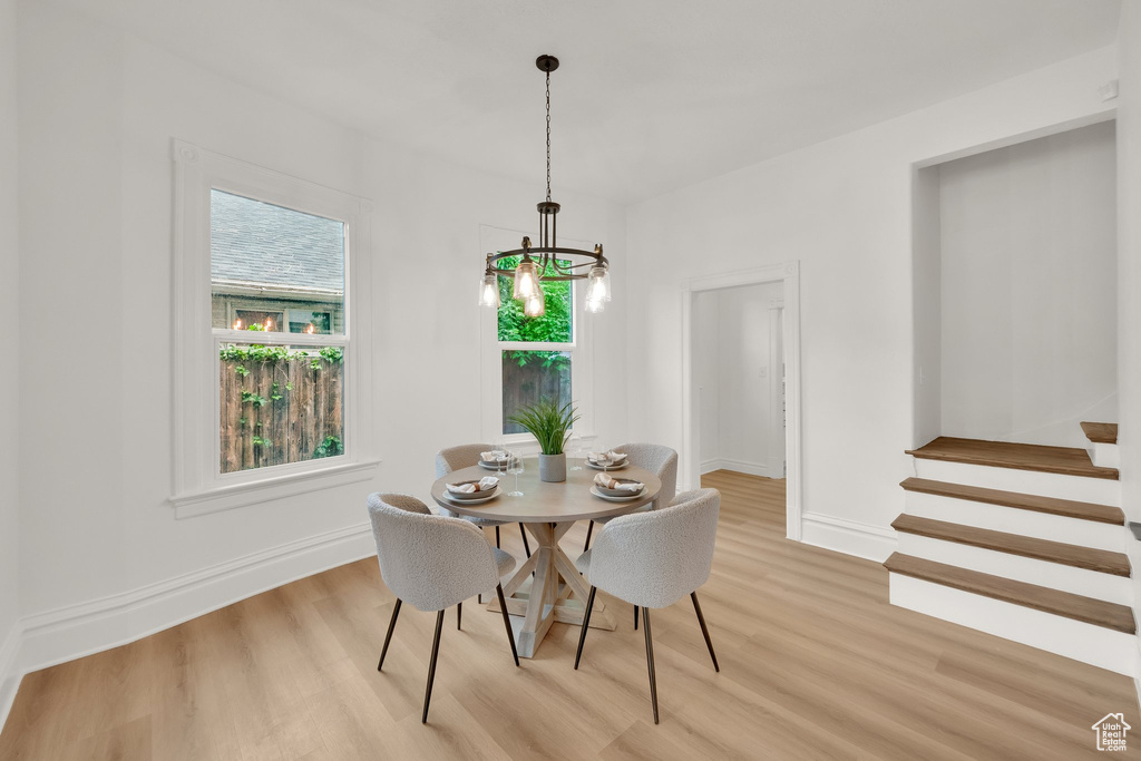 Dining room with light wood finished floors, a chandelier, baseboards, and stairs