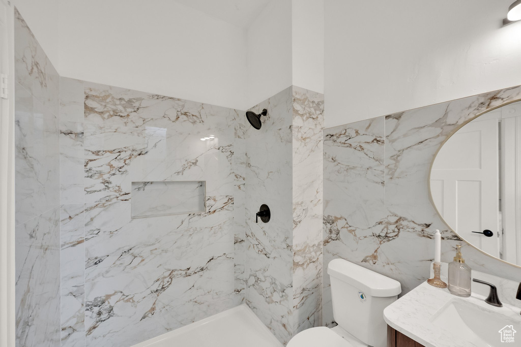 Bathroom featuring vanity, a marble finish shower, toilet, and tile walls