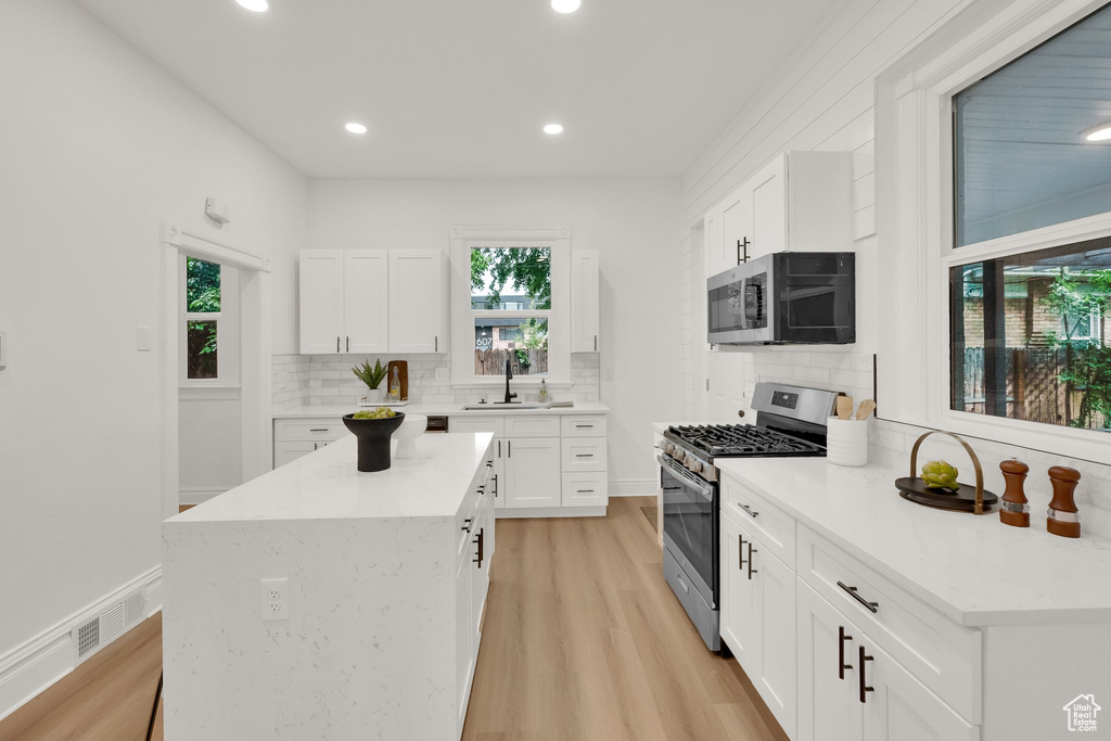 Kitchen with stainless steel appliances, a sink, tasteful backsplash, light wood-style floors, and white cabinetry