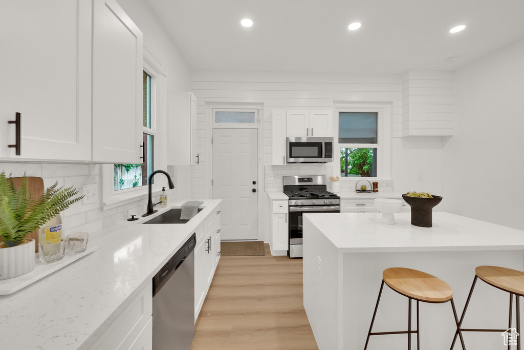 Kitchen with appliances with stainless steel finishes, a sink, a breakfast bar area, white cabinetry, and backsplash
