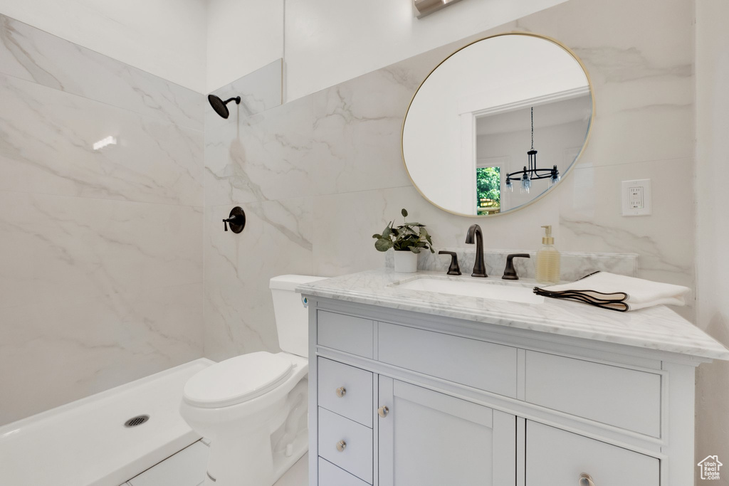 Bathroom with vanity, a marble finish shower, tile walls, toilet, and a chandelier