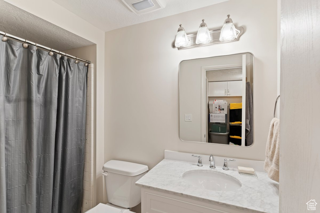 Full bathroom with vanity, toilet, curtained shower, and a textured ceiling