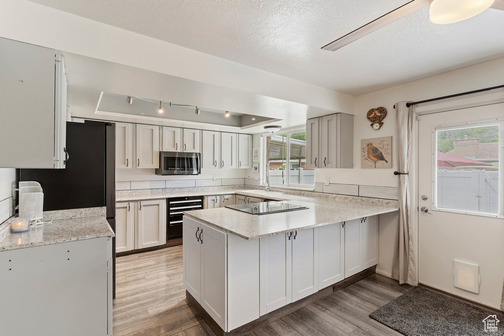 Kitchen featuring stainless steel microwave, a peninsula, light countertops, light wood-style floors, and black electric cooktop