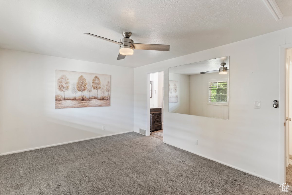 Carpeted spare room with ceiling fan, baseboards, and a textured ceiling