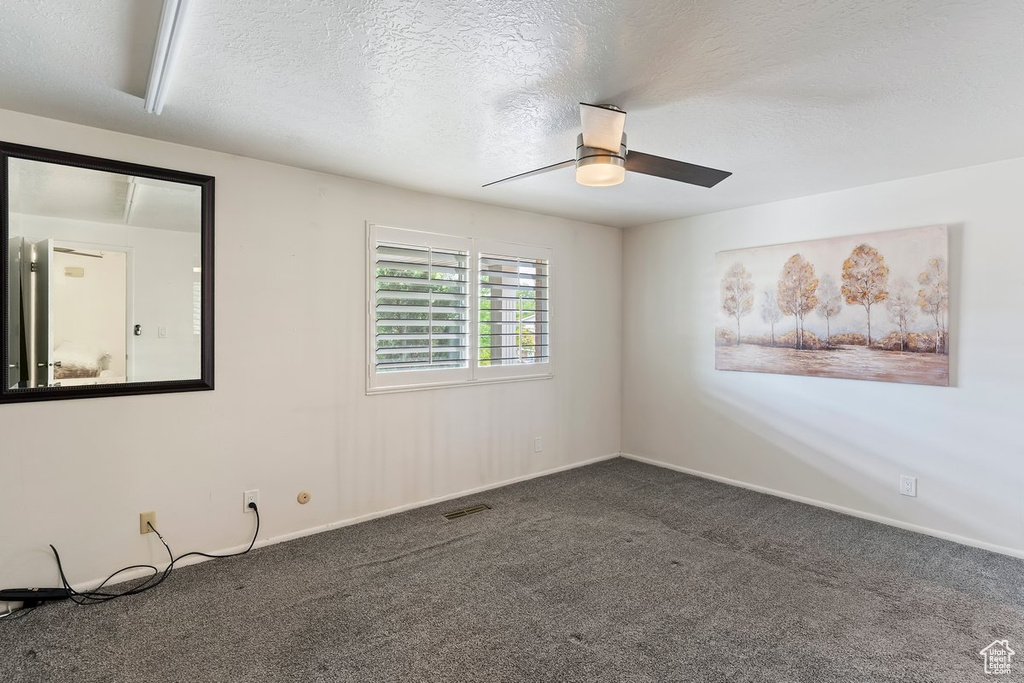 Carpeted spare room with a ceiling fan, baseboards, and a textured ceiling