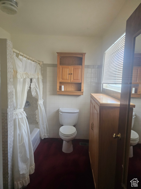 Bathroom featuring toilet, tile walls, shower / bath combination with curtain, and vanity