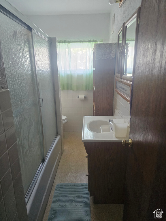 Full bathroom with healthy amount of natural light, tile walls, vanity, toilet, and enclosed tub / shower combo