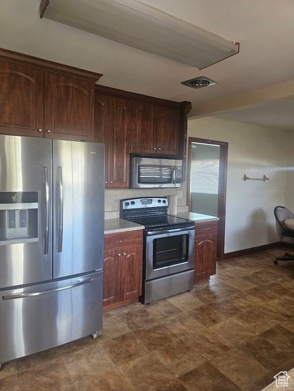 Kitchen with appliances with stainless steel finishes, light countertops, baseboards, and dark brown cabinets