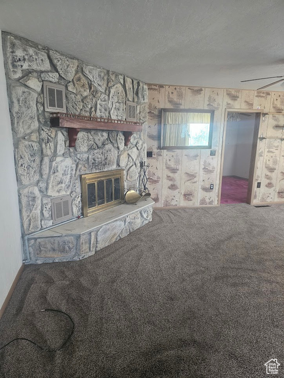Carpeted living area with a stone fireplace and a textured ceiling