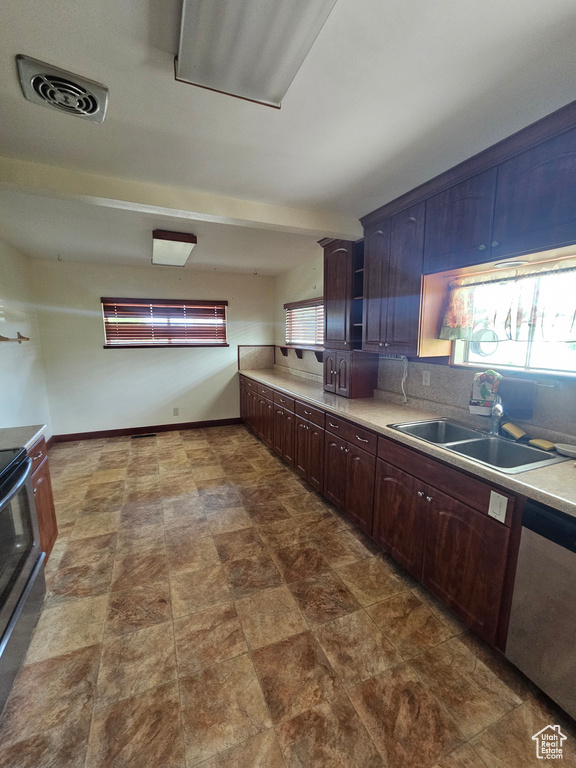 Kitchen featuring a sink, appliances with stainless steel finishes, backsplash, light countertops, and dark brown cabinetry