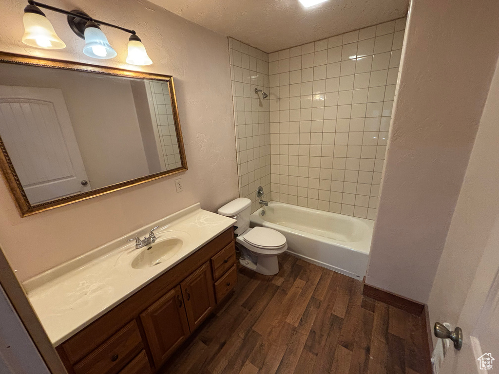 Full bath featuring wood finished floors, toilet, vanity, a textured ceiling, and tub / shower combination