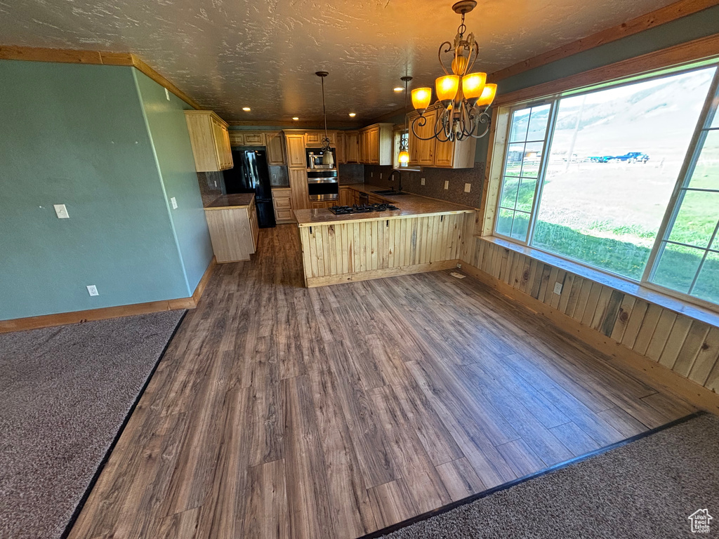 Kitchen featuring black appliances, a chandelier, a sink, dark wood-type flooring, and a peninsula
