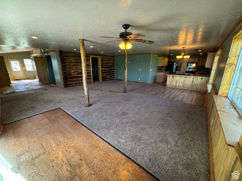 Unfurnished living room with a chandelier, a textured ceiling, carpet flooring, ceiling fan, and wood finished floors