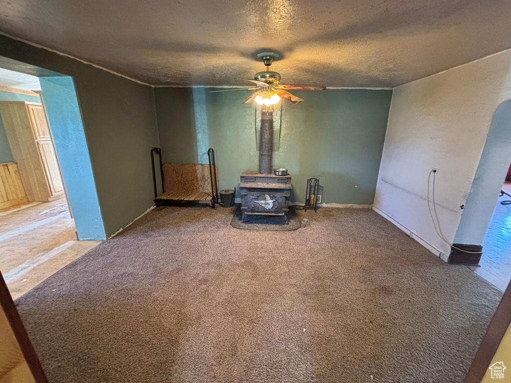 Unfurnished room featuring a wood stove, a ceiling fan, carpet, and a textured ceiling