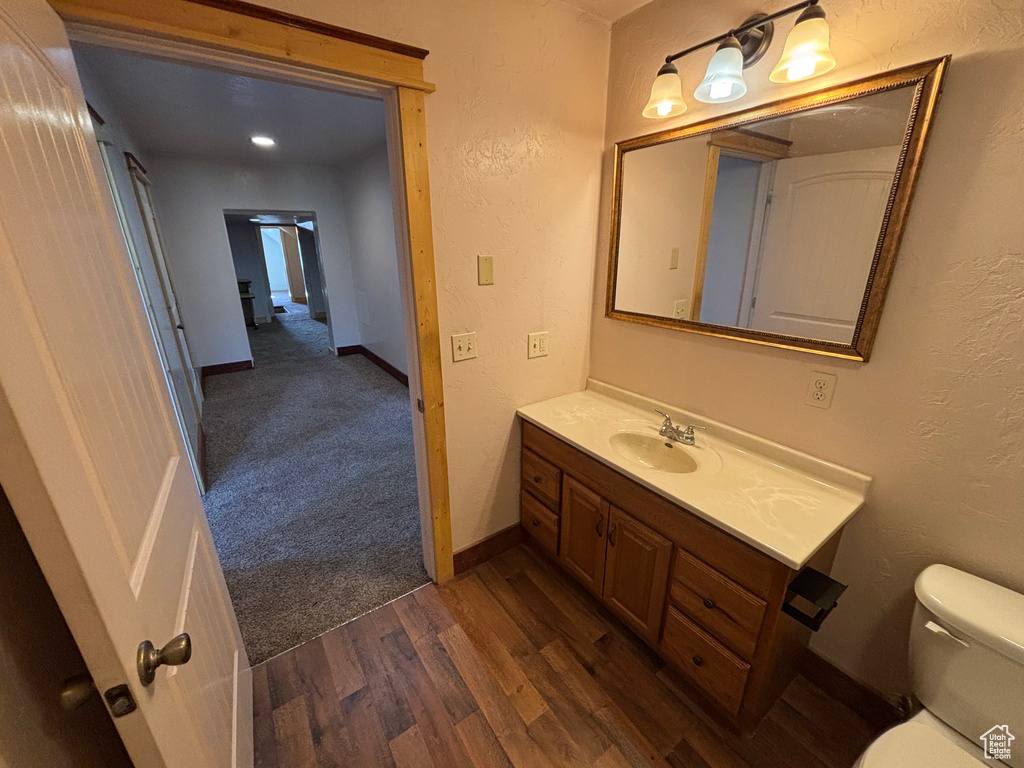 Half bath with vanity, toilet, baseboards, and wood finished floors