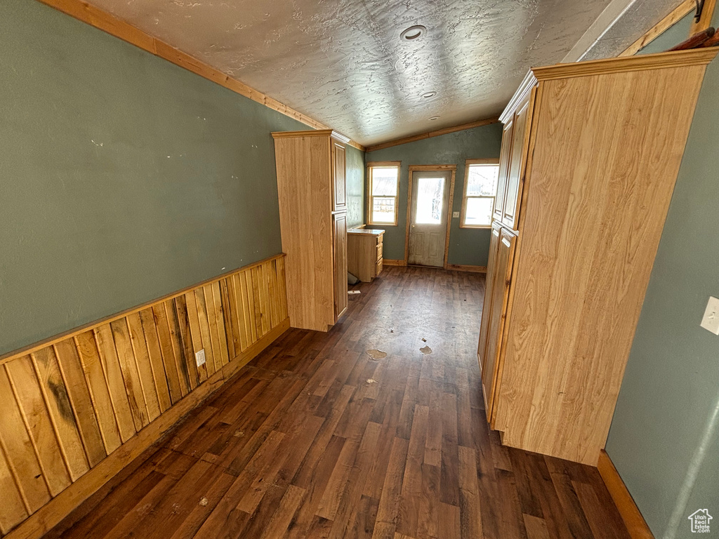 Hallway with vaulted ceiling, dark wood-type flooring, ornamental molding, a wainscoted wall, and wood walls