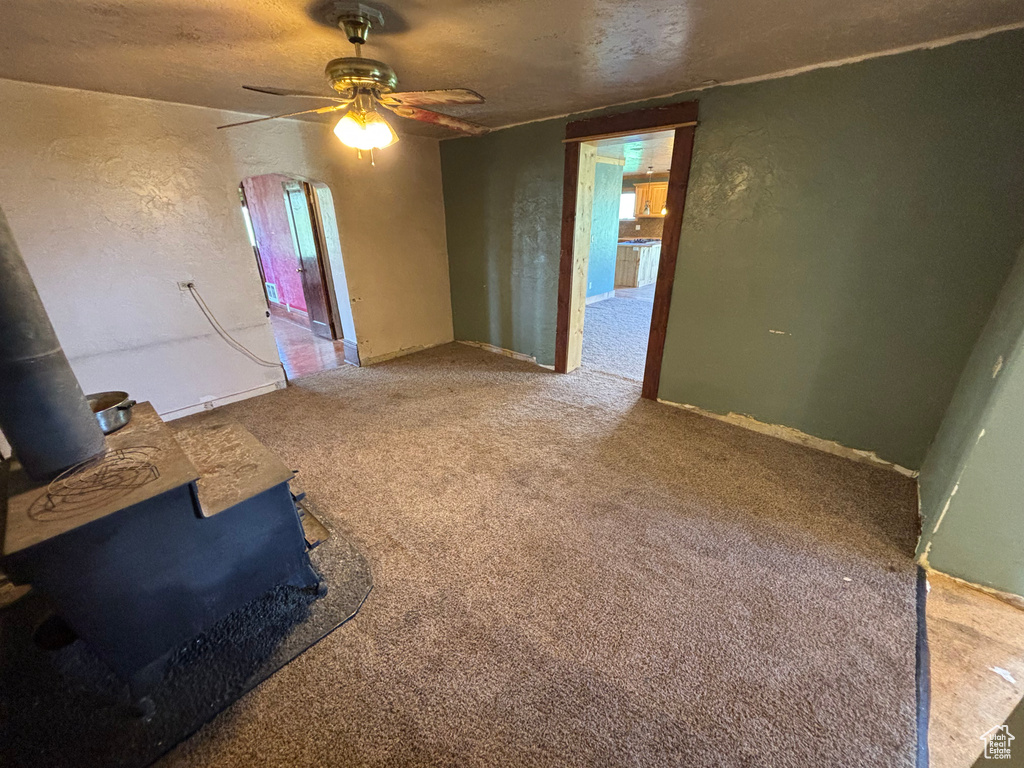 Unfurnished room featuring a wood stove, ceiling fan, carpet flooring, a textured wall, and a textured ceiling