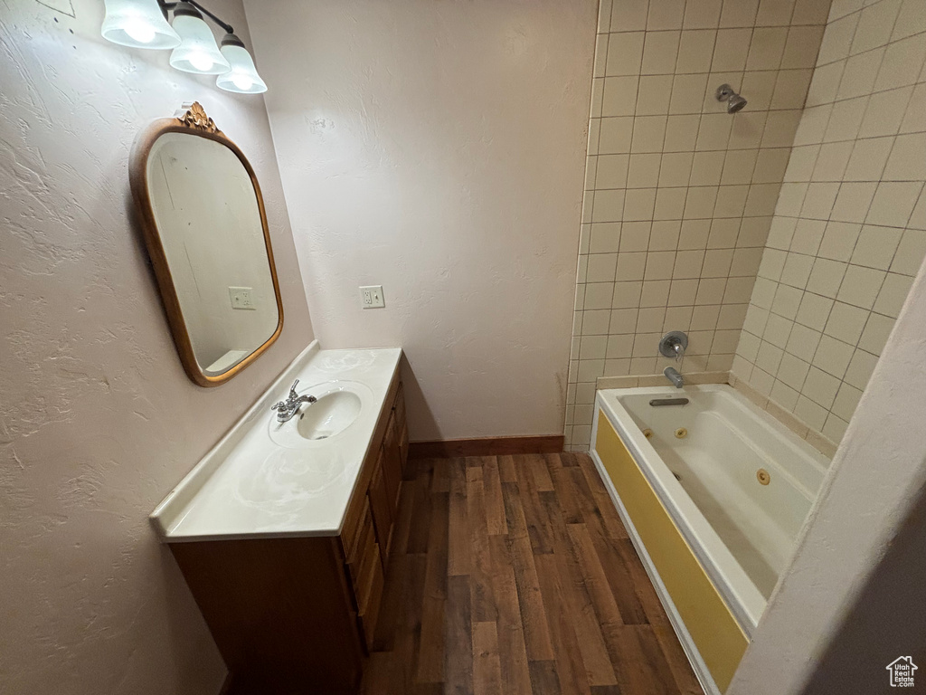 Full bath featuring wood finished floors, vanity, a combined bath / shower with jetted tub, and baseboards