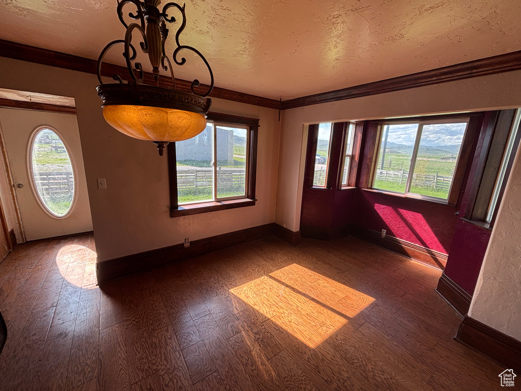 Unfurnished dining area with healthy amount of natural light, wood finished floors, a textured ceiling, baseboards, and ornamental molding
