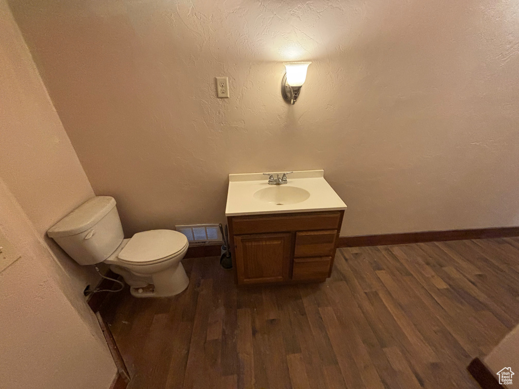 Half bath with vanity, toilet, wood finished floors, and baseboards
