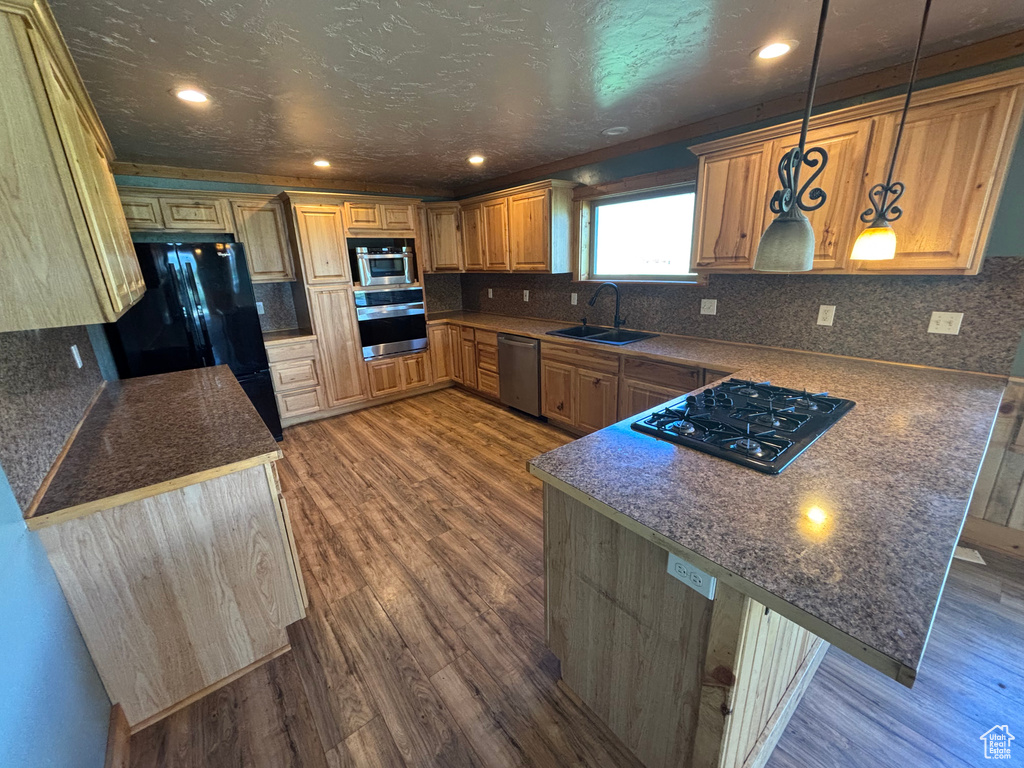 Kitchen with black appliances, a sink, a peninsula, dark wood-style flooring, and tasteful backsplash