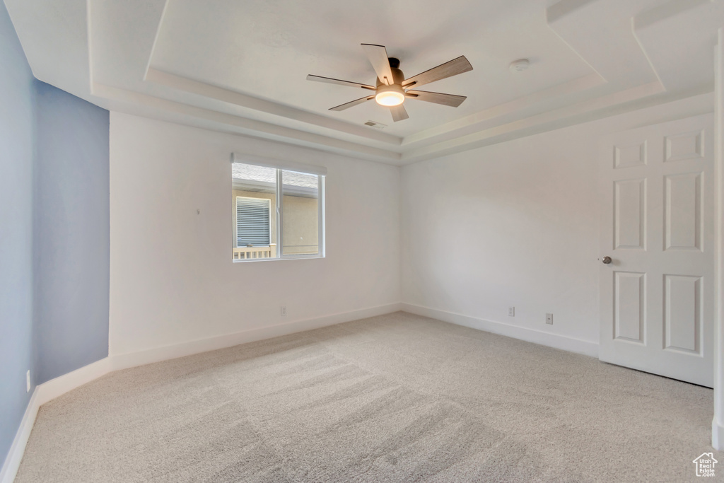 Empty room with a tray ceiling, a ceiling fan, light carpet, and baseboards