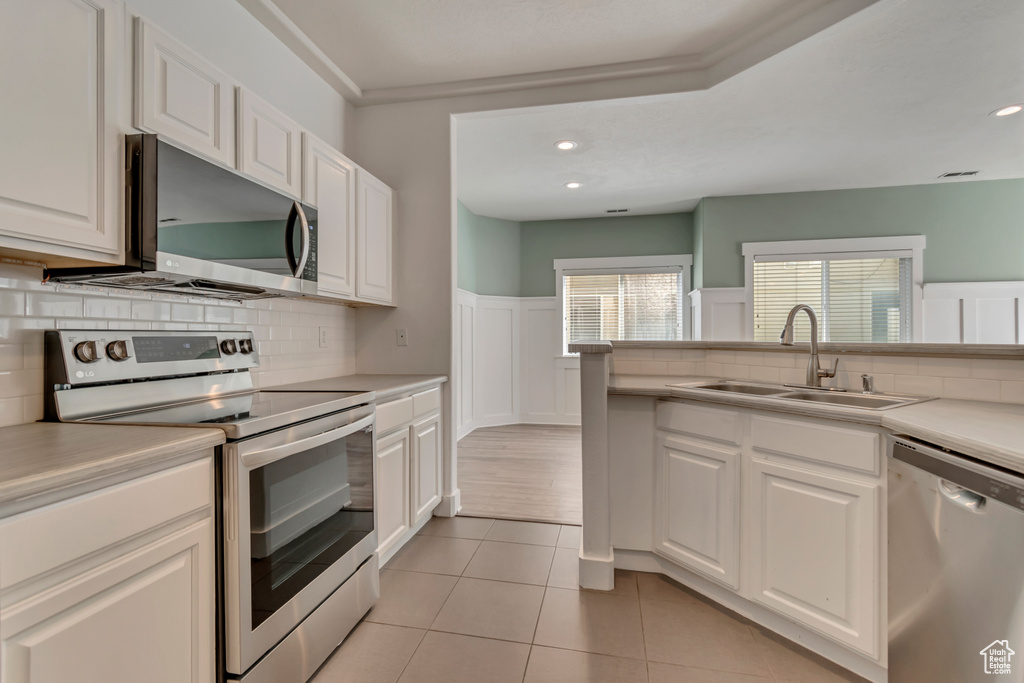 Kitchen with stainless steel appliances, a sink, white cabinetry, light countertops, and wainscoting
