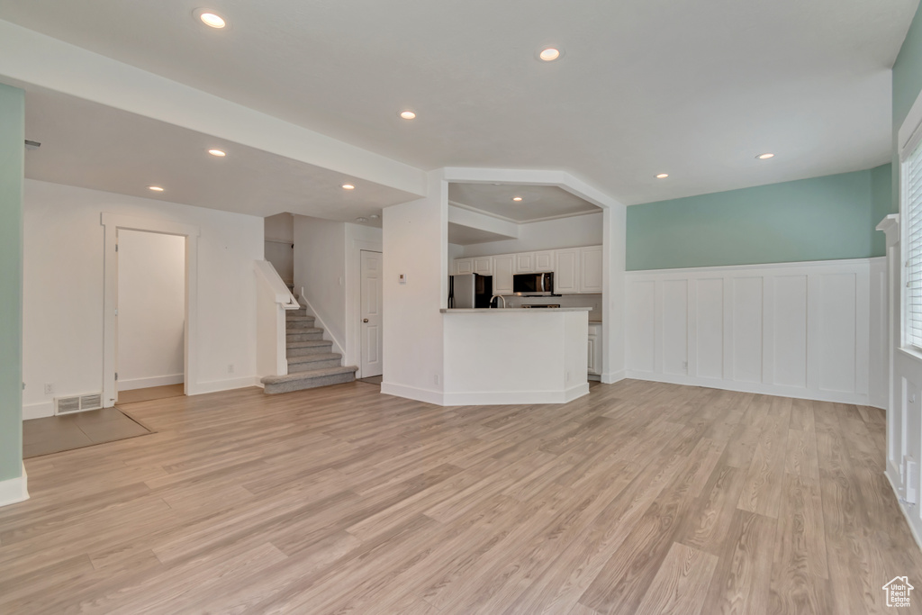 Unfurnished living room with light wood-style floors, stairs, wainscoting, recessed lighting, and a decorative wall