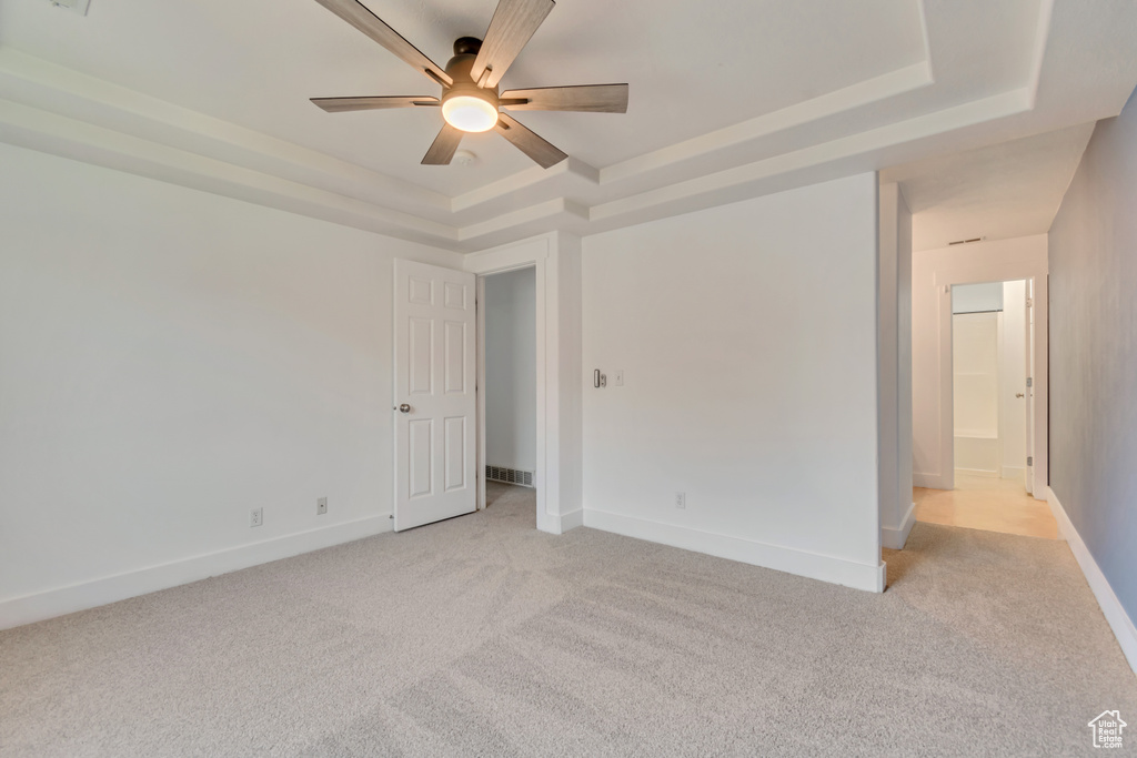 Unfurnished room with a raised ceiling, light carpet, a ceiling fan, and baseboards