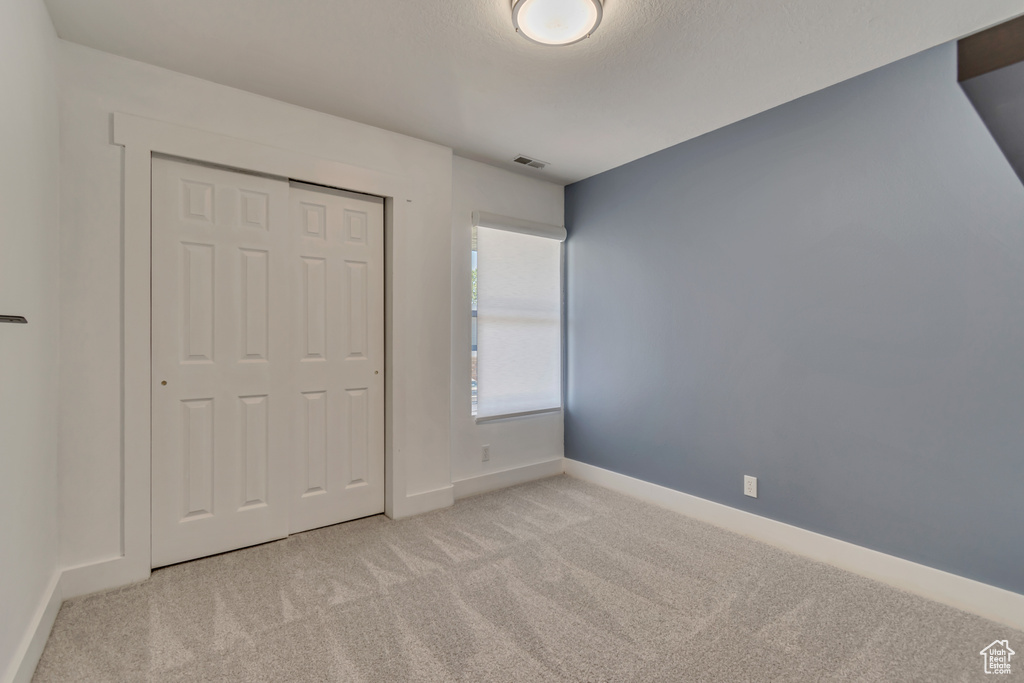Unfurnished bedroom with light colored carpet, baseboards, and a closet