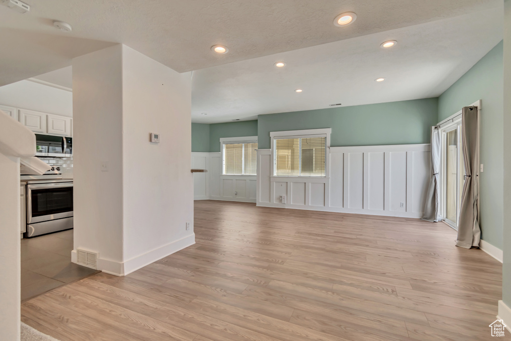 Unfurnished living room with a decorative wall, light wood-type flooring, wainscoting, and recessed lighting
