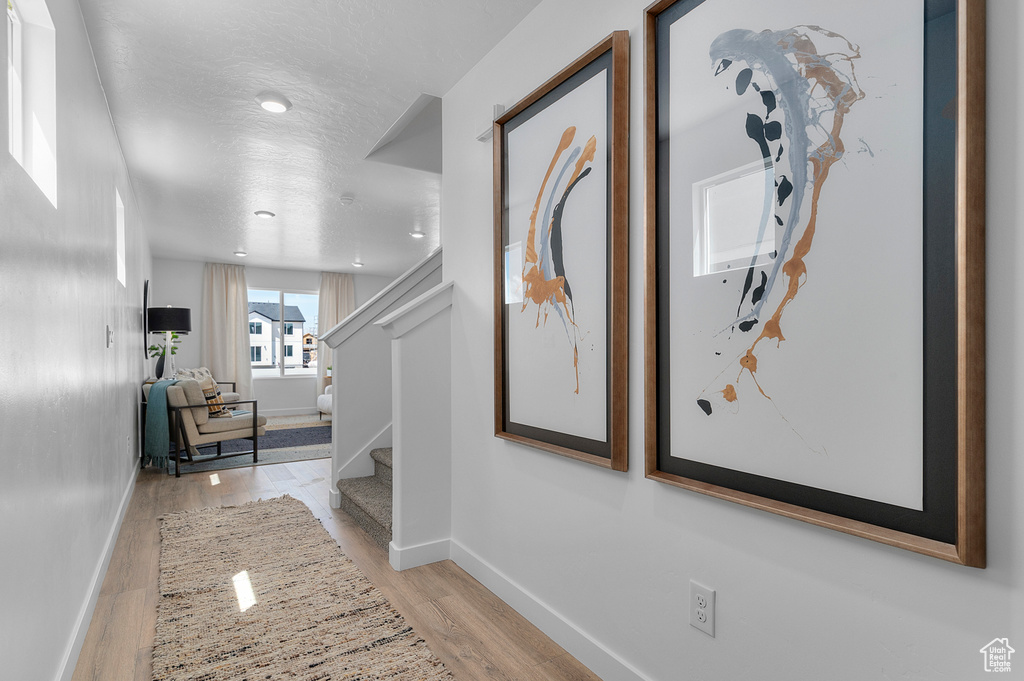 Corridor with light wood-style floors, baseboards, stairway, and a textured ceiling
