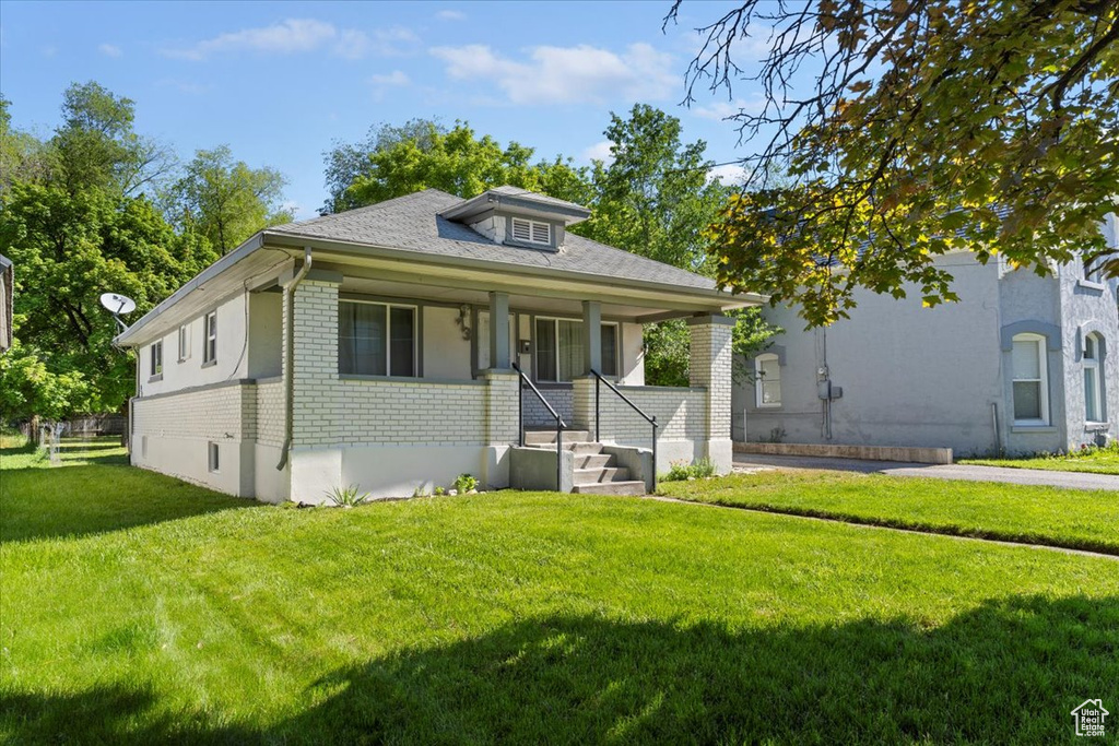Bungalow featuring a front lawn, brick siding, and covered porch
