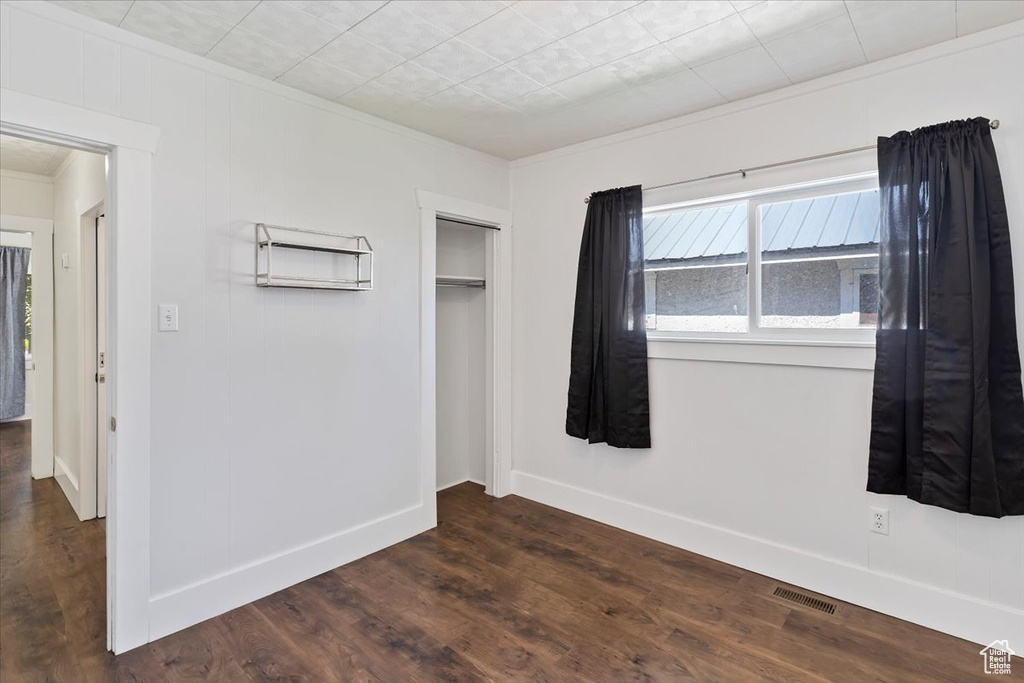 Unfurnished bedroom with crown molding, dark wood-style floors, a closet, and baseboards