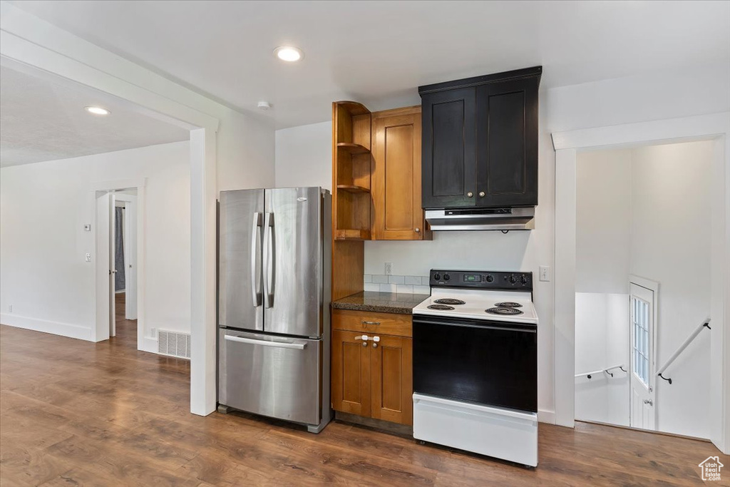 Kitchen featuring electric stove, freestanding refrigerator, under cabinet range hood, dark wood-type flooring, and recessed lighting