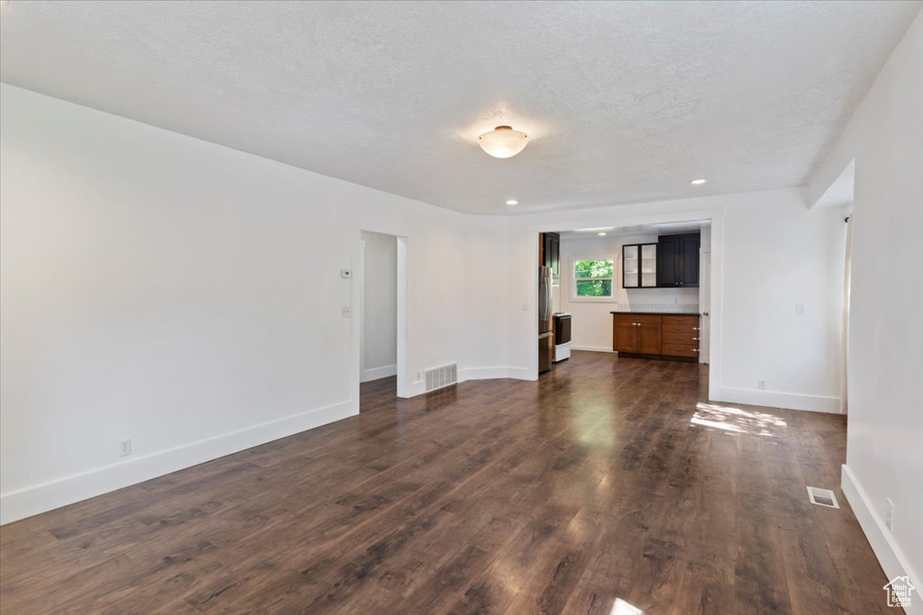 Unfurnished living room featuring dark wood finished floors, baseboards, a textured ceiling, and recessed lighting