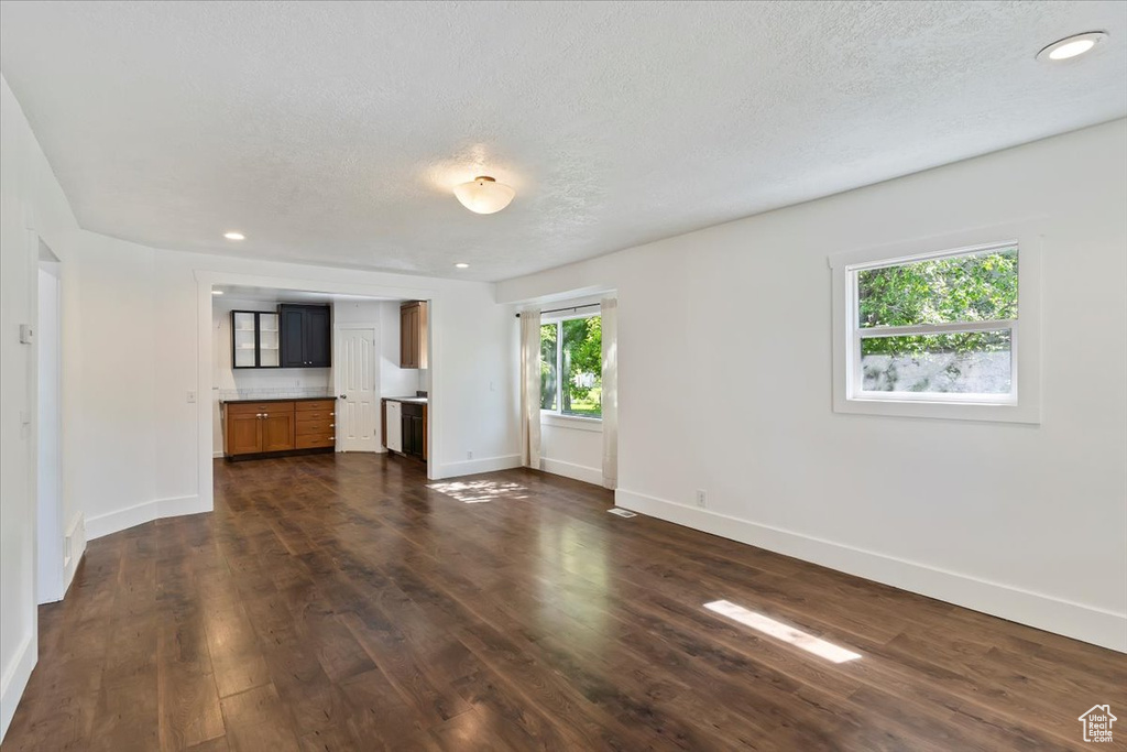 Unfurnished living room featuring baseboards, dark wood-style floors, recessed lighting, and a textured ceiling