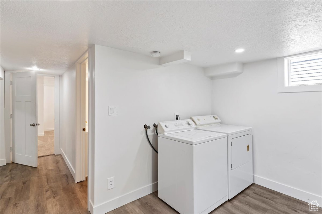 Laundry room featuring a textured ceiling, washing machine and clothes dryer, baseboards, and wood finished floors