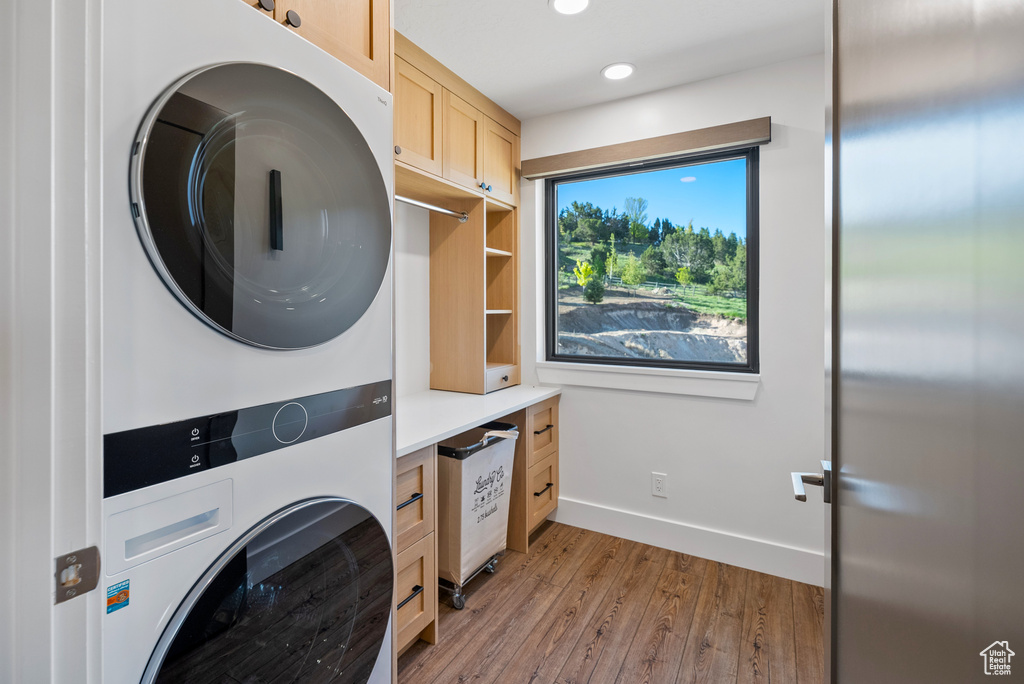 Laundry room featuring stacked washing machine and dryer, cabinet space, light wood finished floors, recessed lighting, and baseboards
