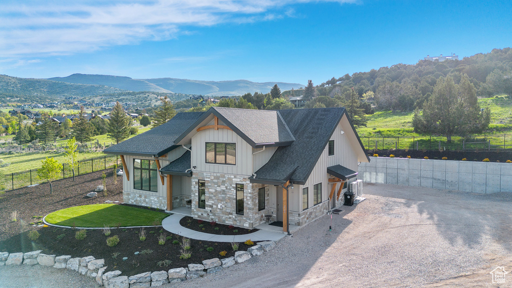 View of front of house with stone siding, driveway, a shingled roof, and a mountain view
