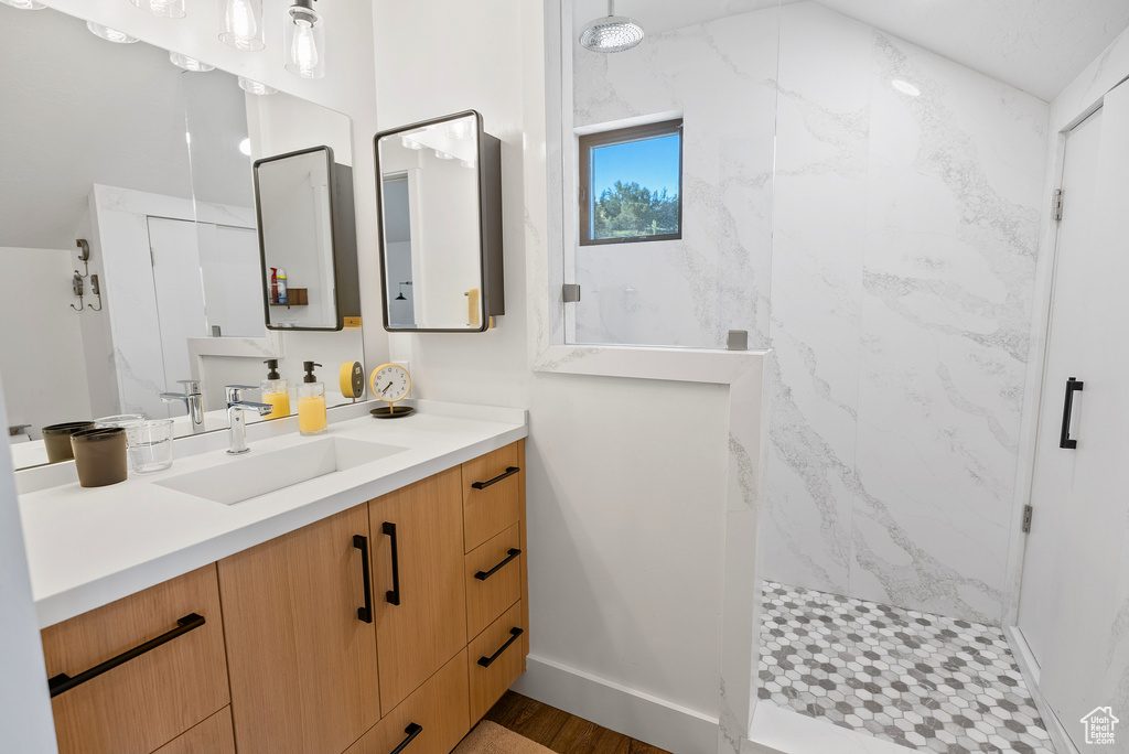 Full bath featuring a marble finish shower, vanity, wood finished floors, and baseboards