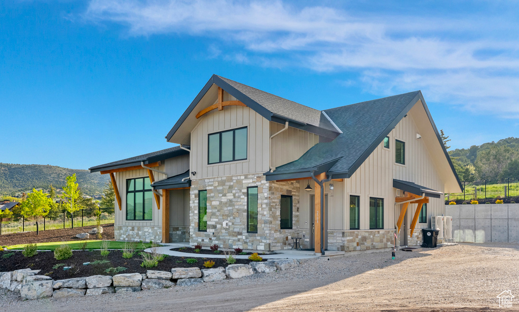 Modern farmhouse with stone siding, a shingled roof, board and batten siding, and a mountain view