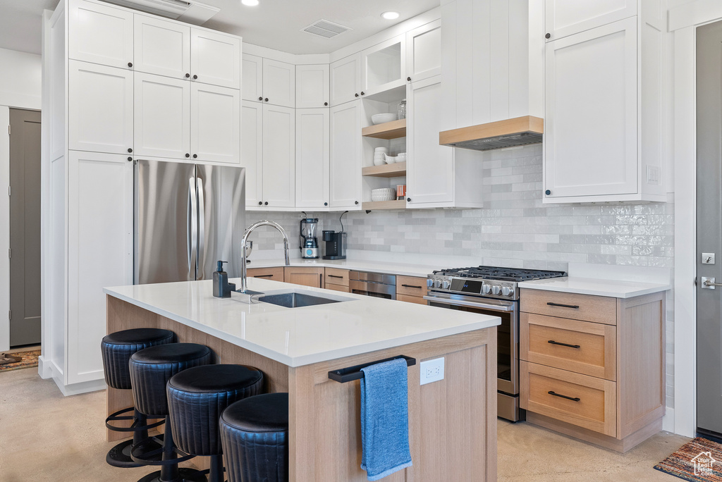 Kitchen with a sink, appliances with stainless steel finishes, a breakfast bar, tasteful backsplash, and light countertops